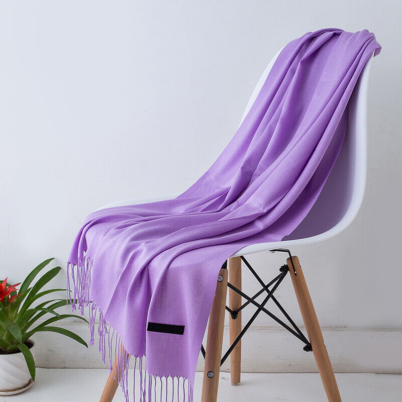 Écharpe en cachemire violet clair drapée sur une chaise moderne en bois, plante verte en pot à côté. Accessoire mode élégant et tendance.