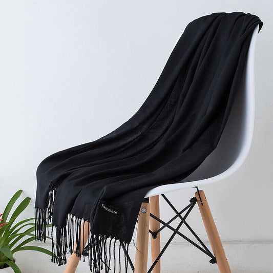 Écharpe en cachemire noire élégamment drapée sur une chaise moderne en bois, avec franges, idéale pour l'hiver et la mode chic.