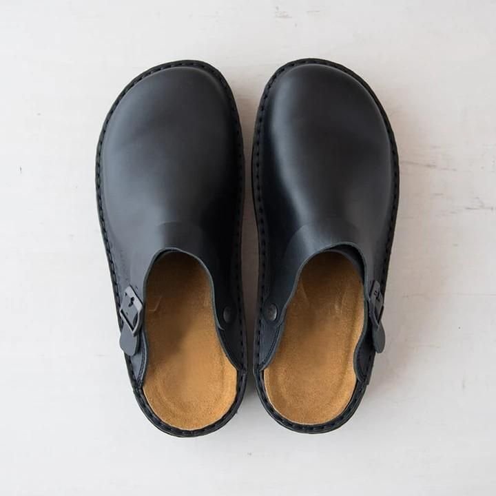 Sabots en cuir noir minimalistes sur fond blanc, design épuré et moderne, parfaits pour un style décontracté et confortable.