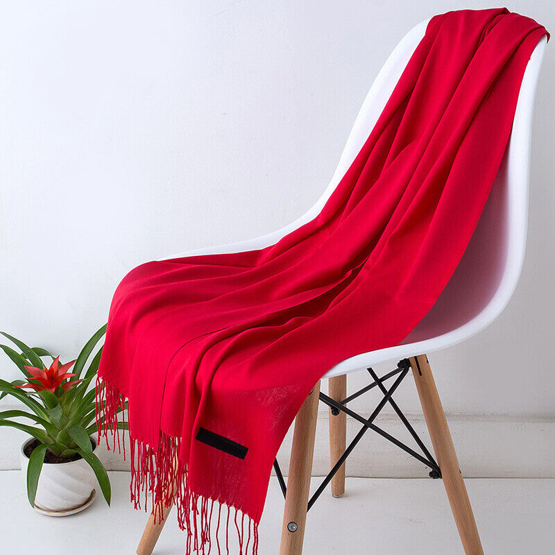 Écharpe rouge en laine sur chaise blanche moderne, plante verte en pot à côté. Accessoire mode élégant, décoration intérieure minimaliste.