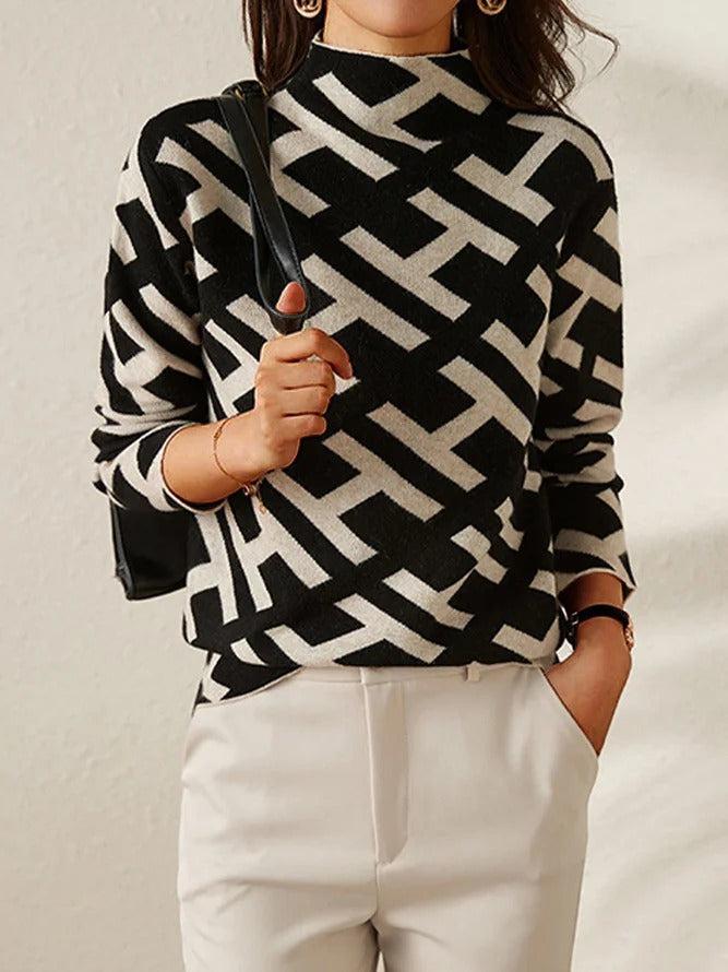 Femme portant un pull à motifs géométriques noir et blanc, sac à main noir, pantalon beige. Mode élégante, style moderne, tenue chic.