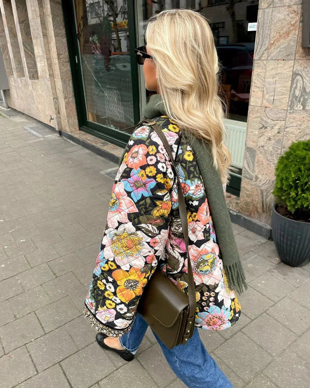 
A stylish women's floral puffer jacket featuring a multicolor design, with a vibrant flower pattern on a quilted fabric, long sleeves, and a high collar.