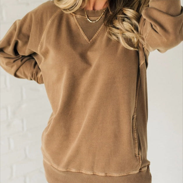 Femme portant un sweat-shirt beige en coton, manches longues, col en V, devant un mur blanc. Mode décontractée, tendance automne-hiver.