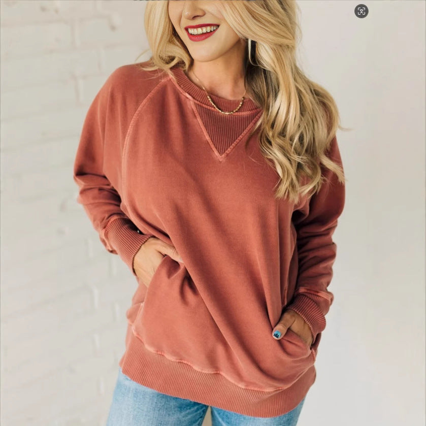 Femme souriante portant un pull rose saumon, manches longues, avec un collier doré, posant contre un mur blanc. Mode décontractée, style automne.