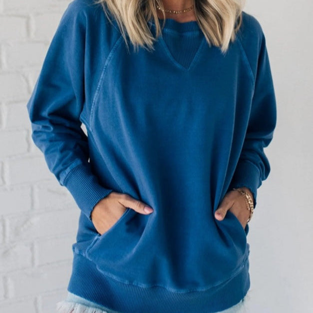 Femme portant un sweat-shirt bleu, manches longues, col rond, devant un mur blanc. Mode décontractée, tendance automne-hiver, style confortable.