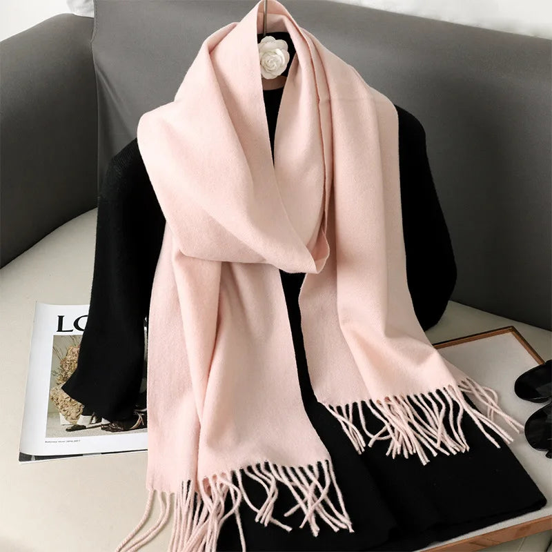 Lyserød kashmir tørklæde med frynser draperet over sort trøje på sofa. Elegant og stilfuldt tilbehør til vintermode.