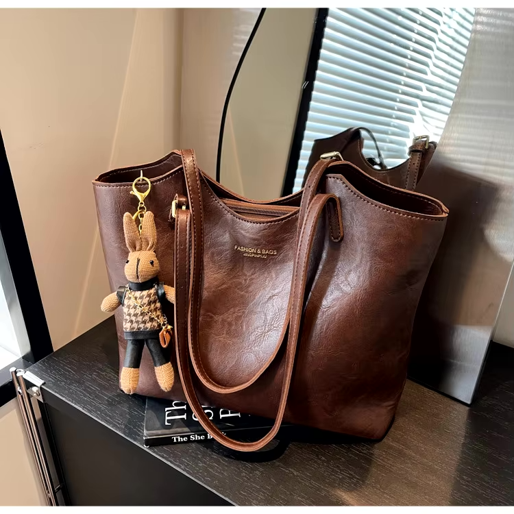 Sac à main en cuir marron avec porte-clés peluche lapin, posé sur une table noire près d'une fenêtre. Accessoire mode élégant et tendance.
