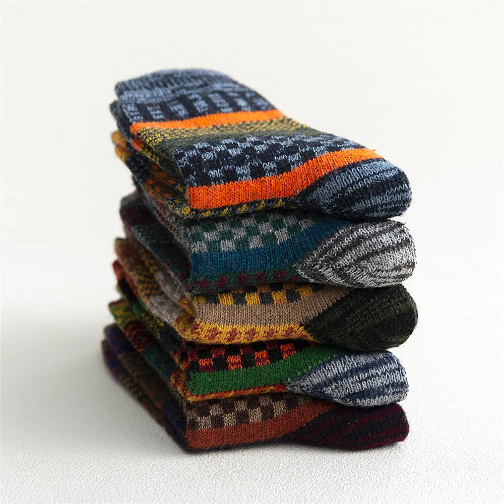 Farverige uldsokker i et mønstret design stablet på hvid baggrund. Vintertilbehør, varmende sokker, strikmode, hygge.