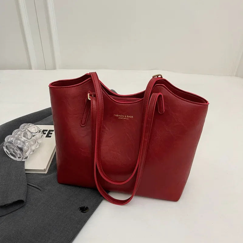 Sac à main rouge élégant en cuir, posé sur une veste grise, avec un livre et des lunettes transparentes à côté. Accessoire mode femme chic.