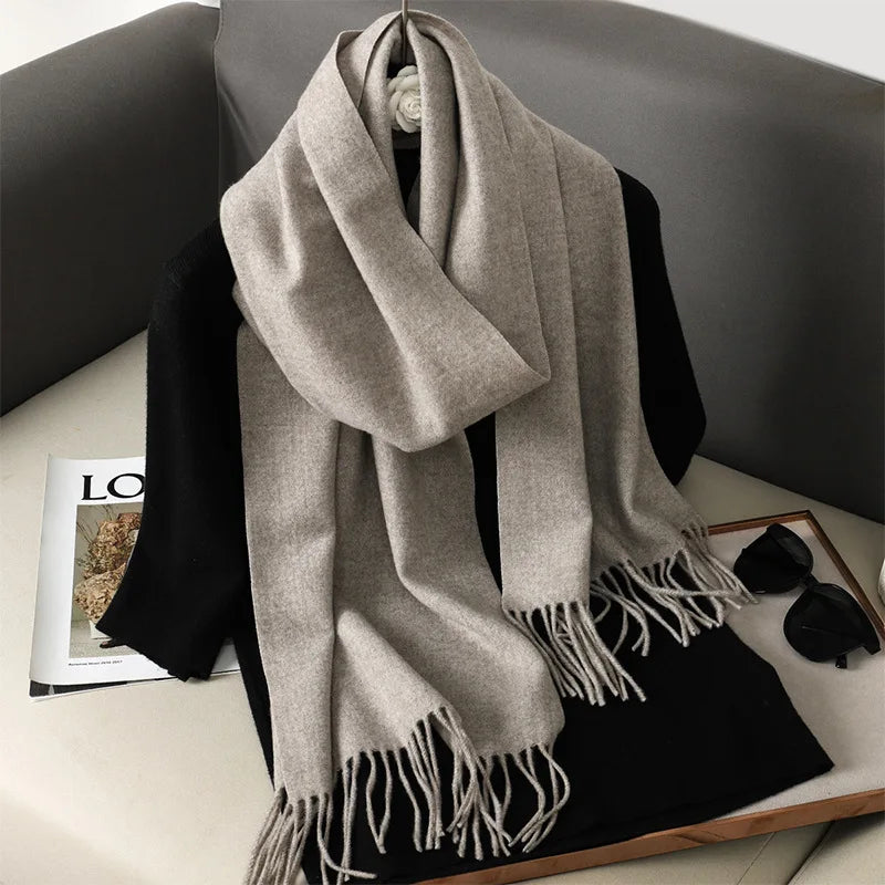 Beige uldtørklæde med frynser på sort trøje, placeret på grå sofa. Perfekt til efterårsmode og vinterstil. Luksuriøst og varmt tilbehør.
