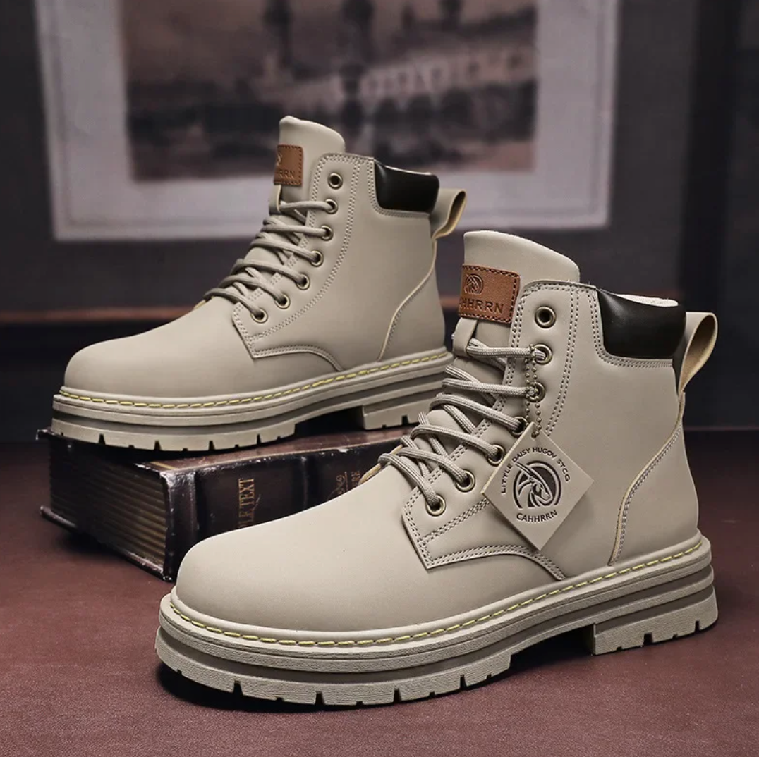 Bottes de randonnée beige pour homme, en cuir, semelle épaisse antidérapante, lacets robustes, étiquette de marque, posées sur des livres anciens.