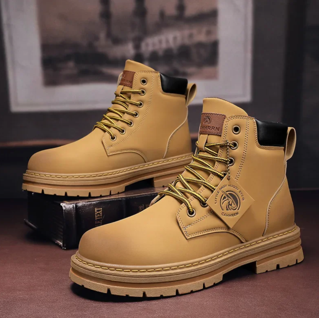 Bottes de travail en cuir marron clair pour hommes avec lacets, semelle épaisse antidérapante, étiquette de marque, posées sur une boîte dans un intérieur.