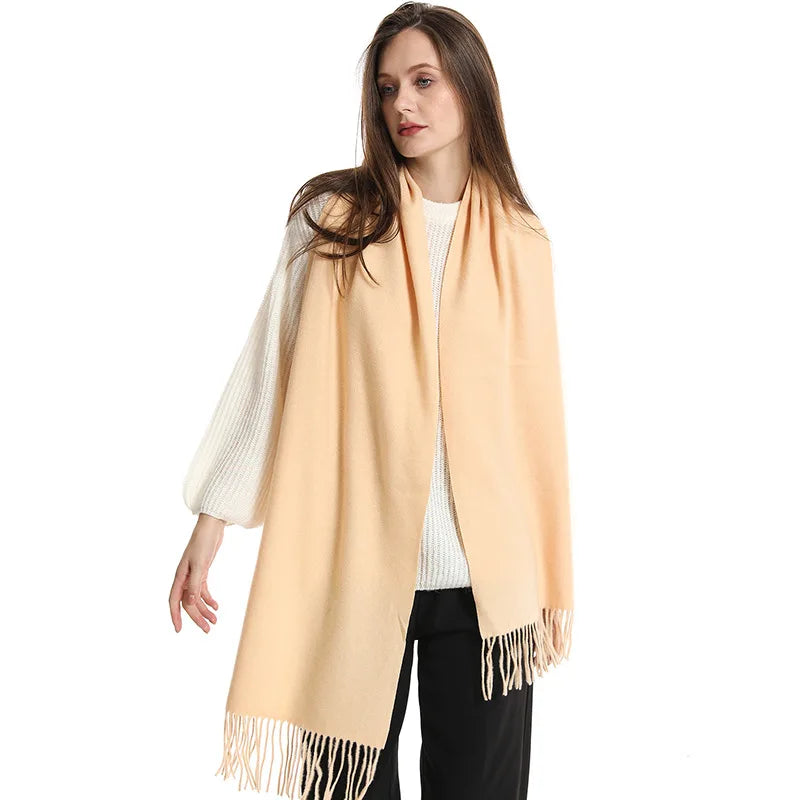 Kvinde iført en lys beige cashmere tørklæde med frynser, hvid sweater og sorte bukser. Elegant mode, vintertilbehør, stilfuldt look.