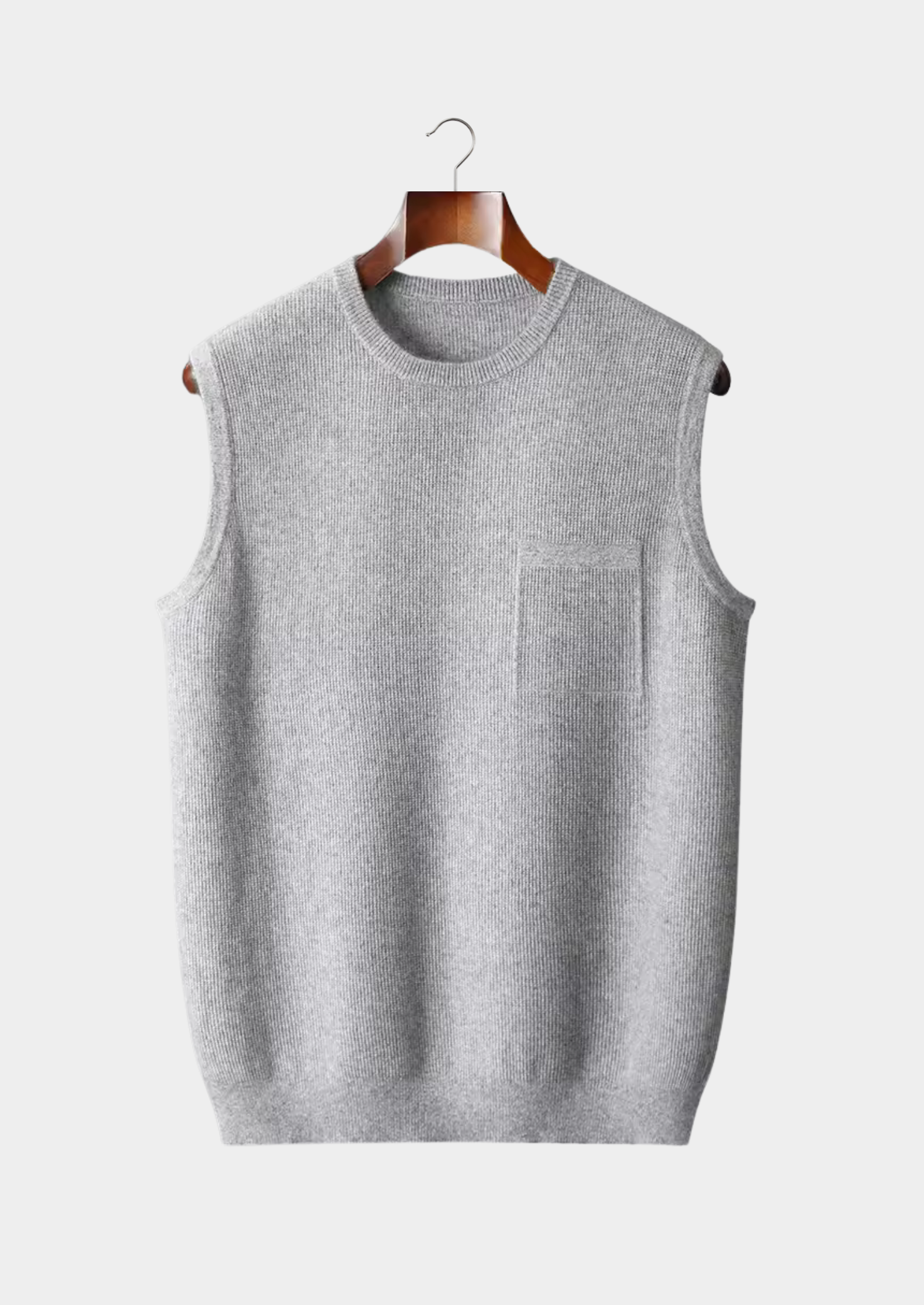 Gilet sans manches gris en tricot, suspendu sur un cintre en bois, avec poche poitrine. Mode homme, vêtement d'hiver élégant et confortable.