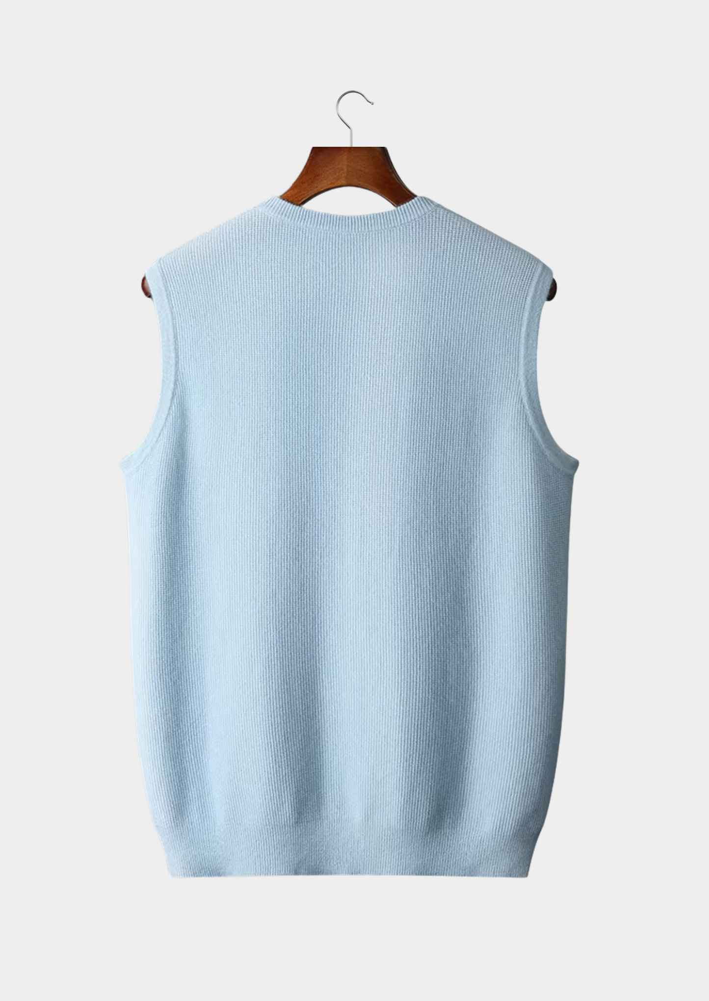Gilet sans manches bleu clair en tricot, suspendu sur un cintre en bois, fond blanc. Mode homme, vêtement décontracté, tendance automne-hiver.