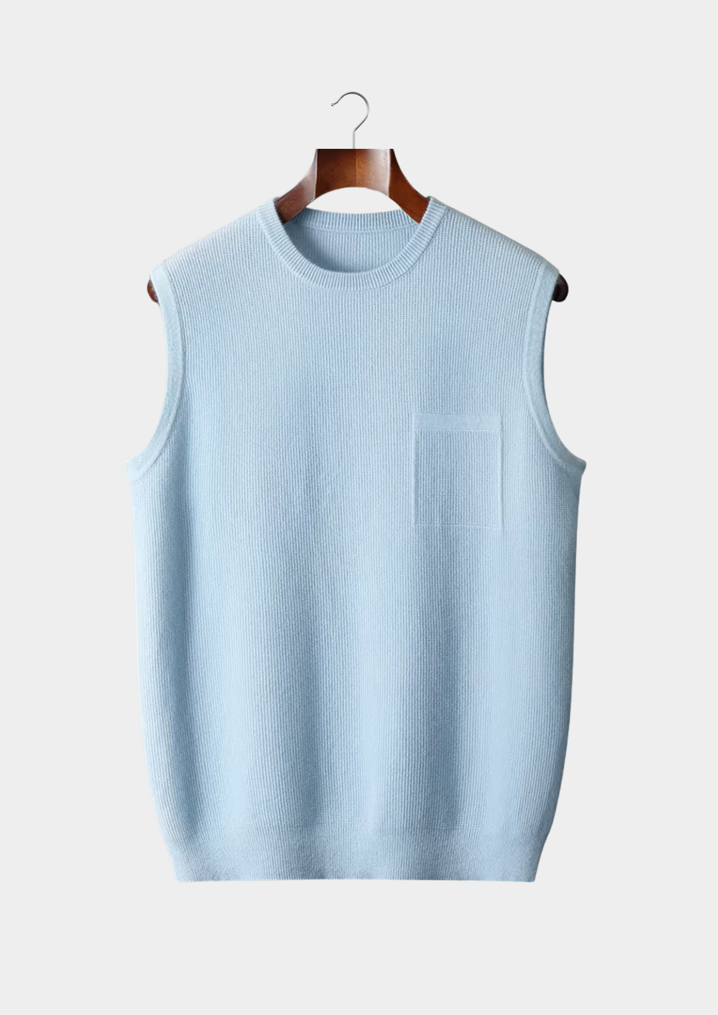 Gilet sans manches bleu clair en tricot, suspendu sur un cintre en bois, fond blanc. Mode homme, vêtement décontracté, tendance automne-hiver.