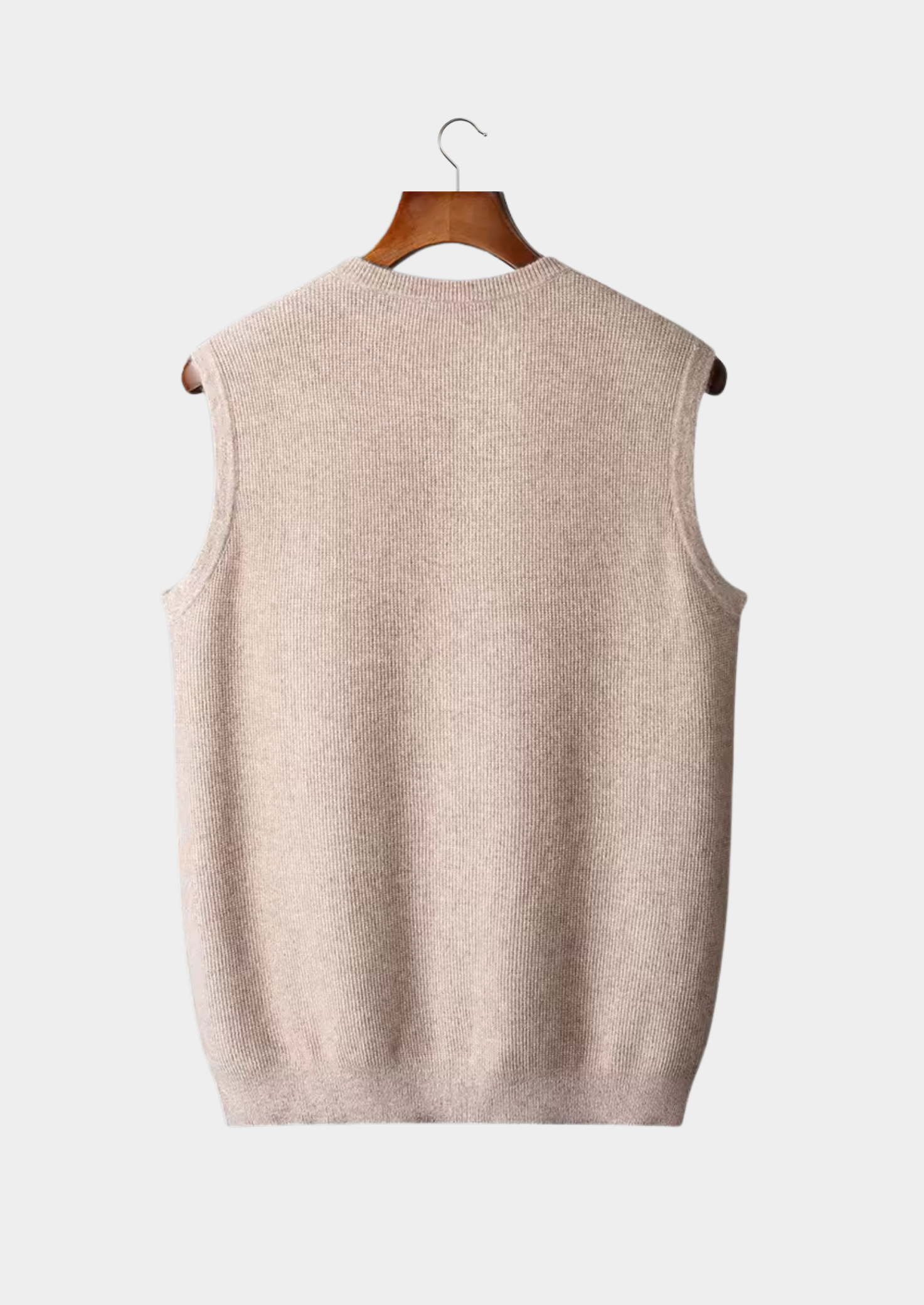 Gilet sans manches en tricot beige suspendu sur un cintre en bois, fond blanc. Mode automne-hiver, vêtement chaud et élégant pour homme.
