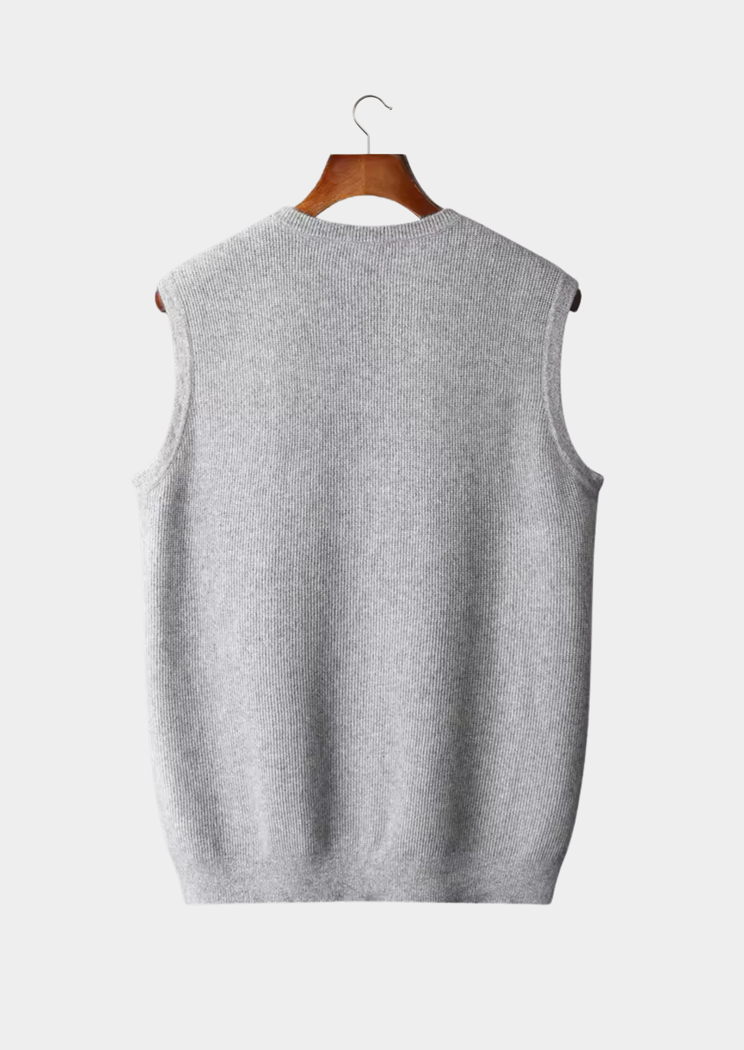 Gilet sans manches gris en tricot, suspendu sur un cintre en bois, fond blanc. Mode automne-hiver, vêtement chaud et élégant.